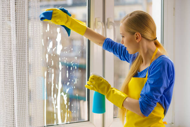 Young woman in yellow gloves cleaning window pane at home with rag and spray detergent. Cleaning concept